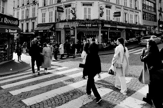 Carrefour parisien en noir et blanc, passants traversant sur les pavés